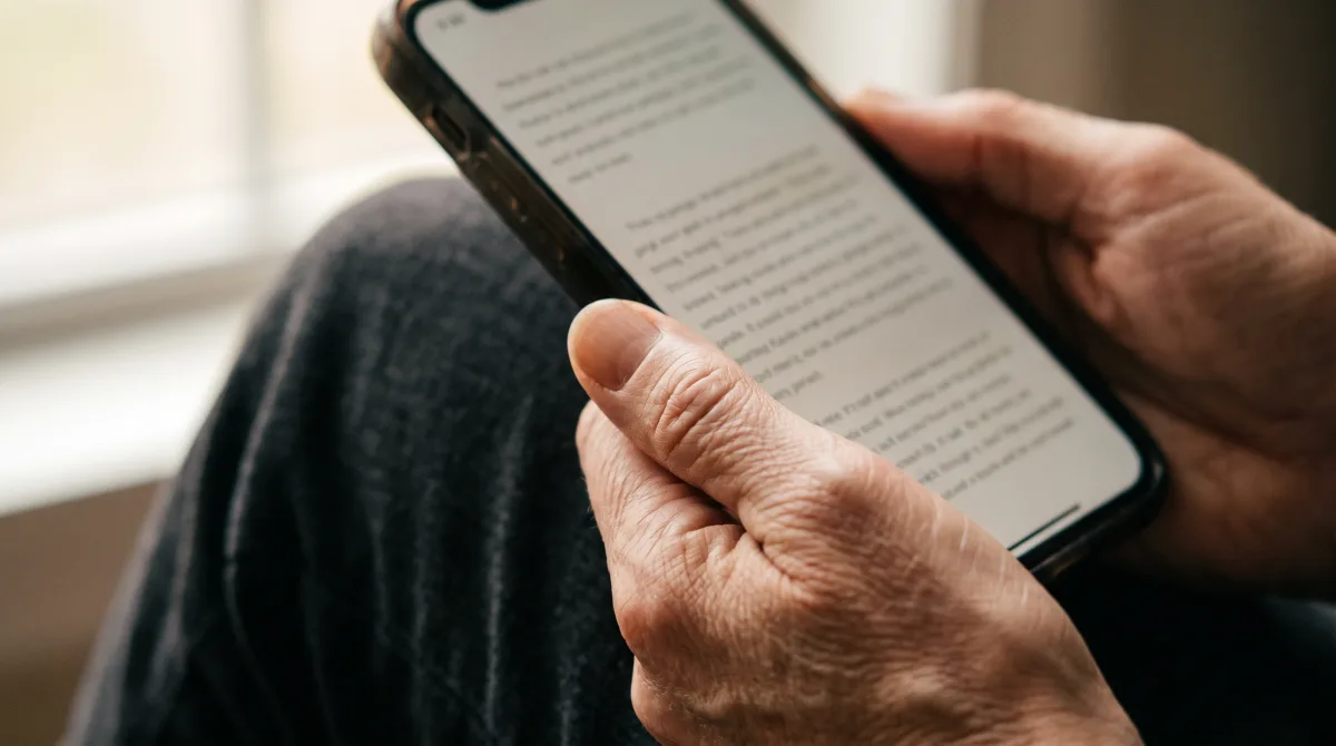 Hands cradling a phone with the thumb resting still instead of mid-swipe, reading calmly by soft light