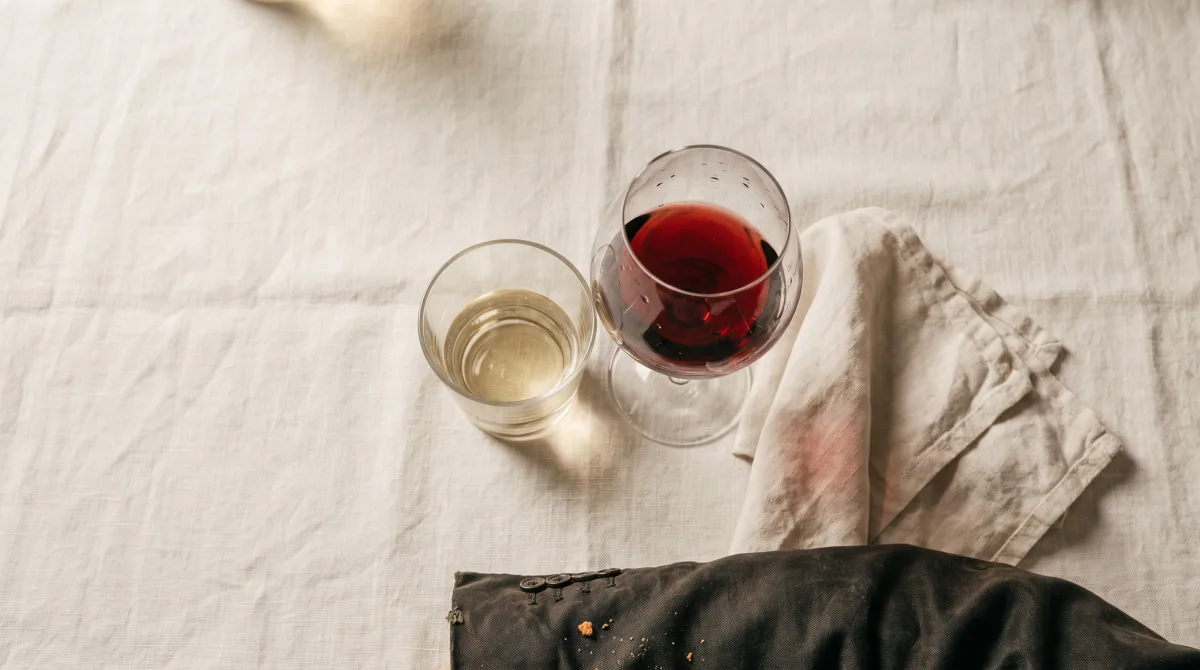 Two drinking glasses set down close together on a linen tablecloth, viewed from above