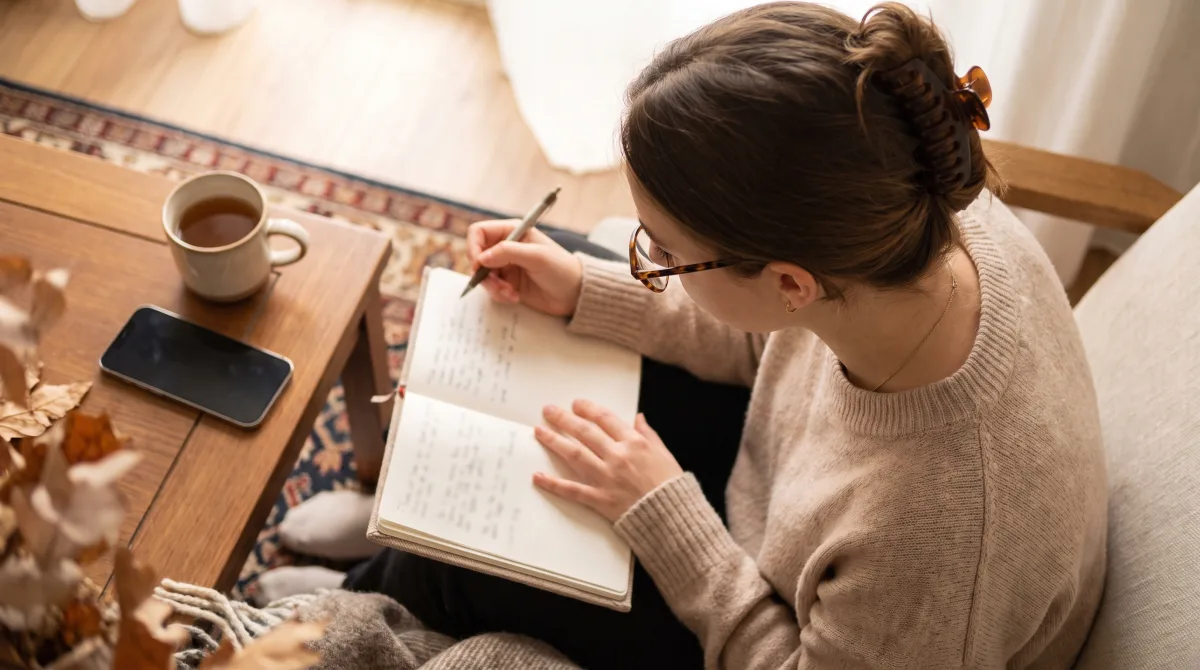 Overhead view of a young woman journaling with a pen in a cozy nook, a cup of tea beside her, reflective and calm
