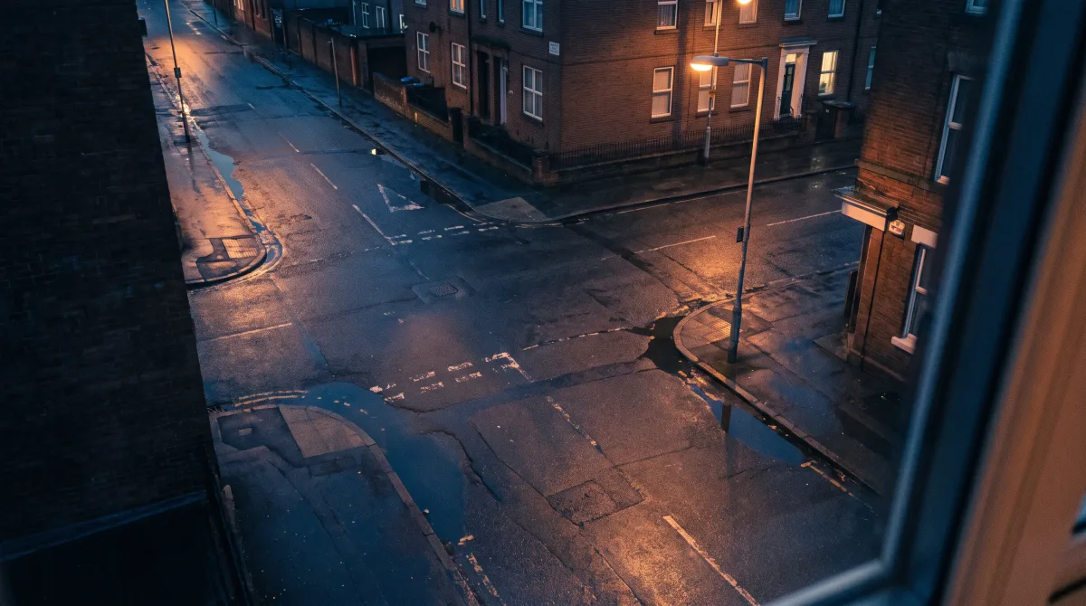 A deserted city intersection seen from above at dusk, wet tarmac holding warm reflections