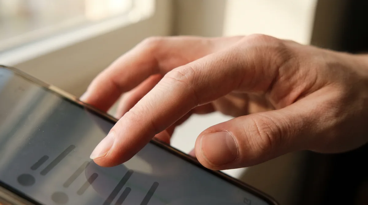 Extreme close-up of a fingertip tracing a single underlined line of text on a phone screen, the rest of the manuscript still out of focus