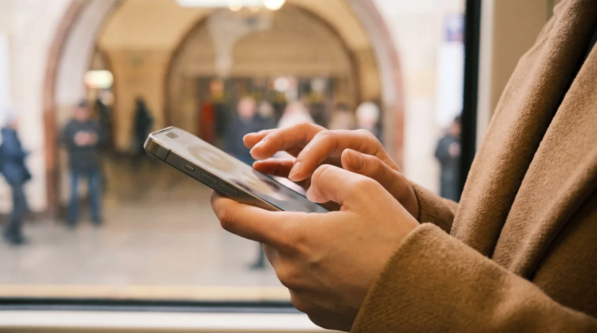 Close-up of young thumbs mid-type on a phone showing a softly blurred chat in a metro car