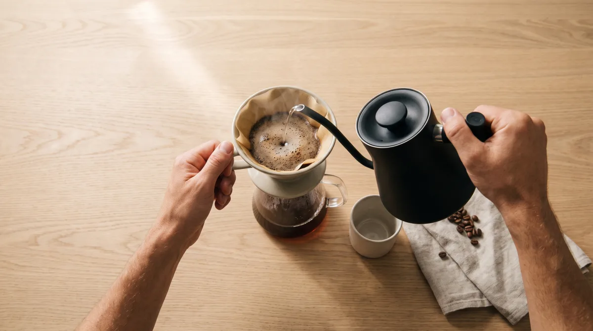 Overhead view of a slow pour into a filter, two hands and a kettle, no faces in frame
