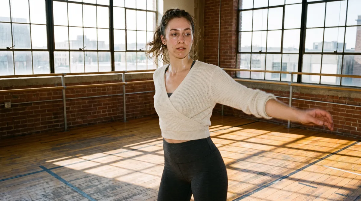 A dancer mid-turn in a sun-filled studio, motion blur trailing her arm, tall windows and a barre in the background