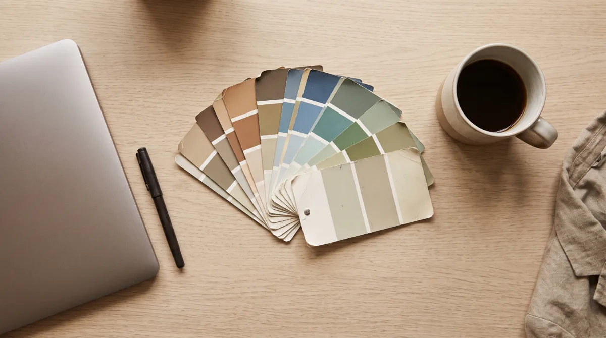 A designer's desk covered in fanned paint swatches beside a half-drunk cup of coffee