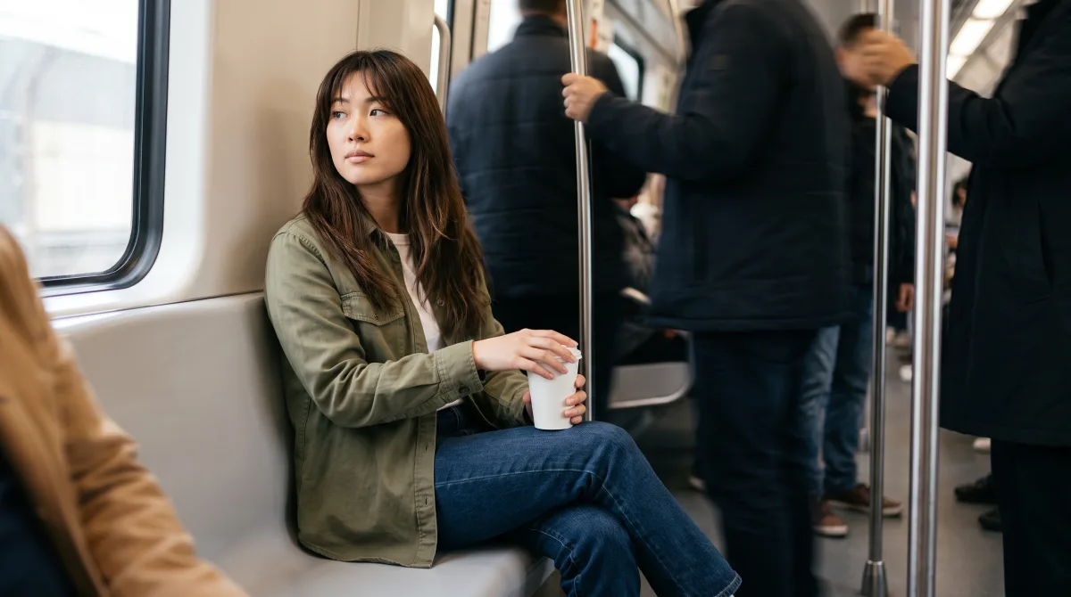 A woman sits alone on a crowded metro car, lost in thought while other passengers blur past around her