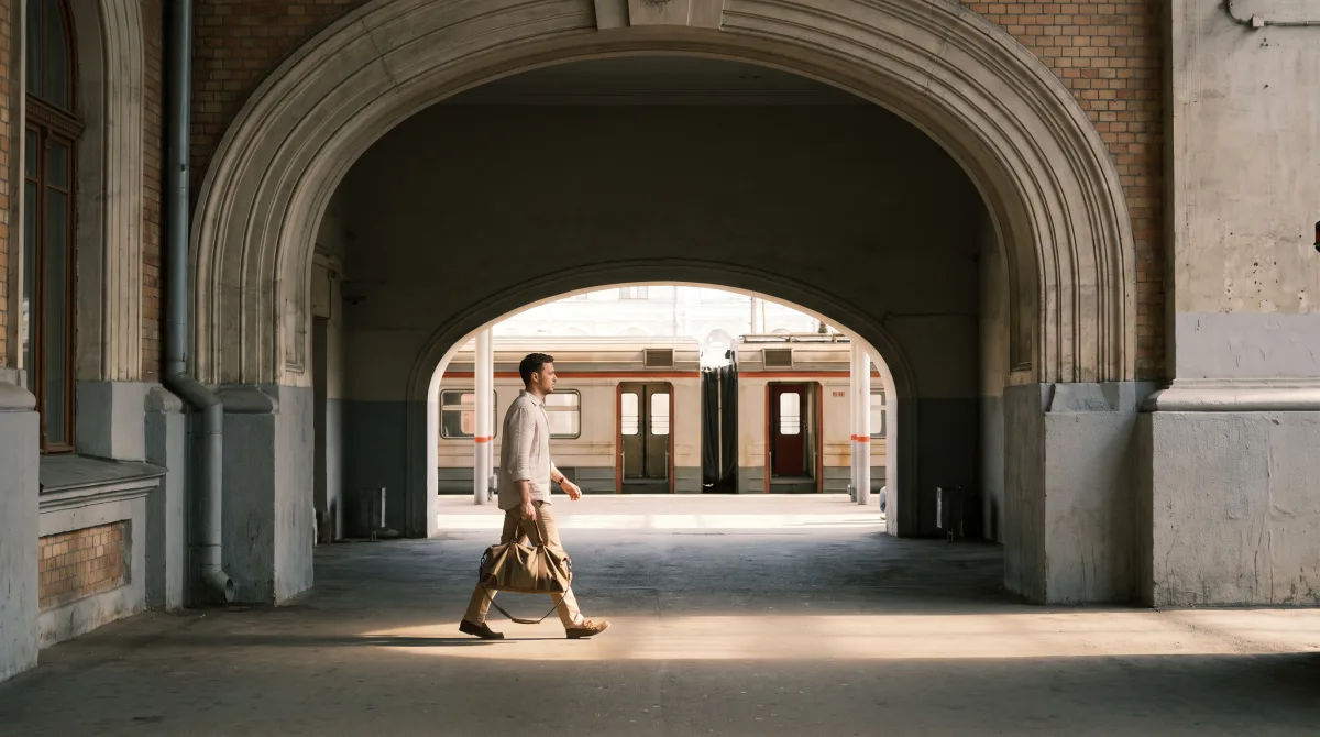 A traveler stepping onto a train under a station platform arch, mid-stride, dwarfed by the architecture