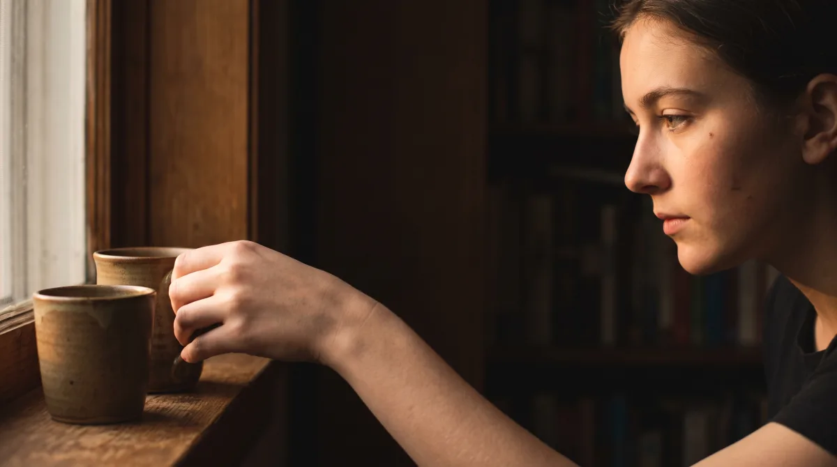 Two hands setting a cup down beside another on a window sill in the evening, warm light, chest height