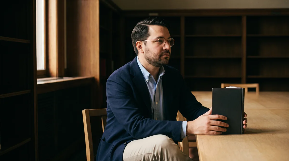 A man sitting alone in a library reading room, head tilted as if listening closely