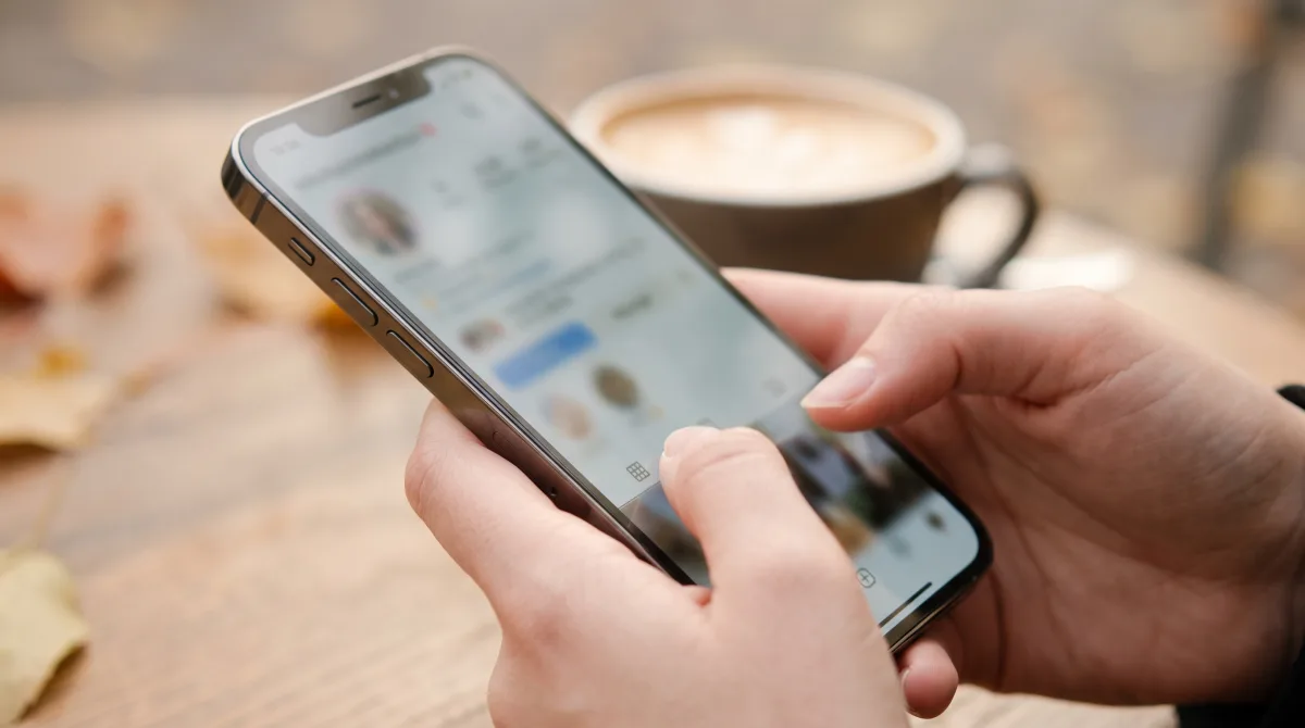 Close-up of young bare hands holding a phone showing a softly blurred profile being scrutinized at a café table