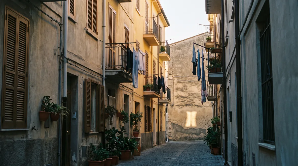A narrow European side street in warm late-afternoon light, shuttered windows and balconies, no one in frame