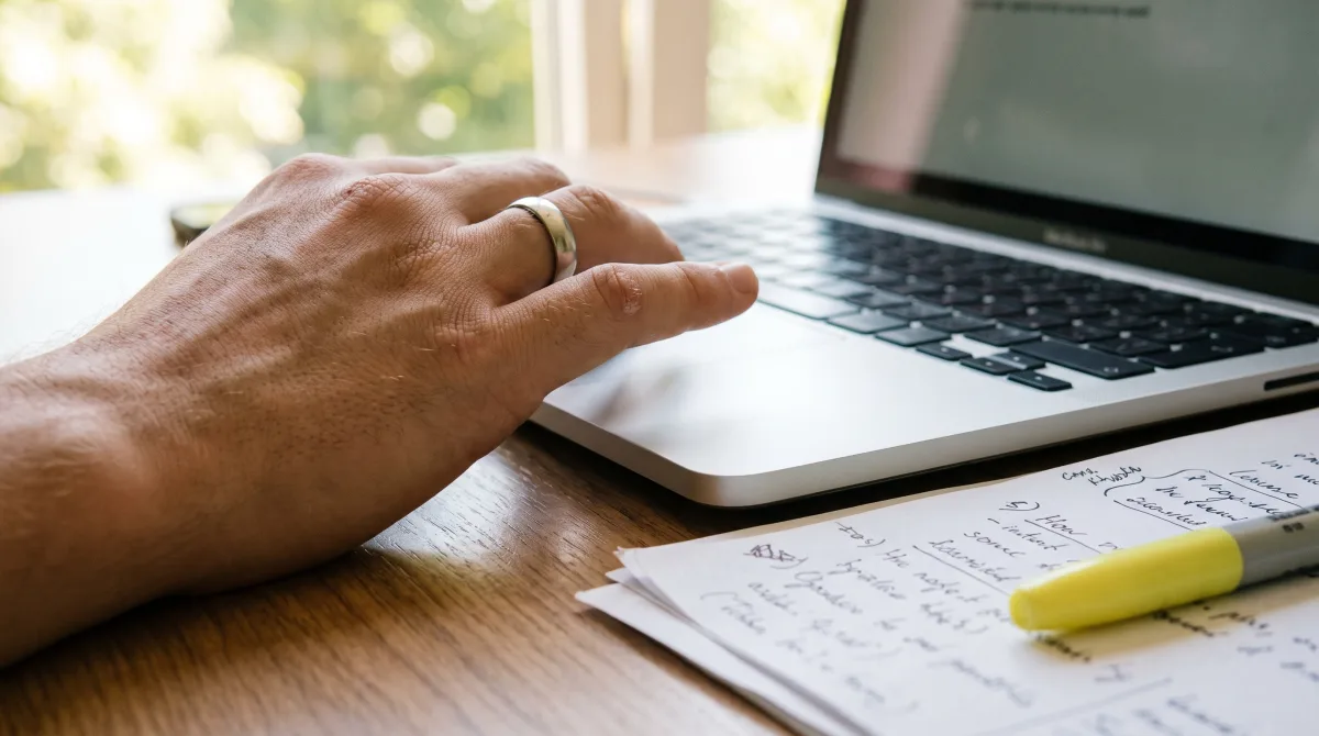 Close-up of a hand on a laptop trackpad beside annotated papers
