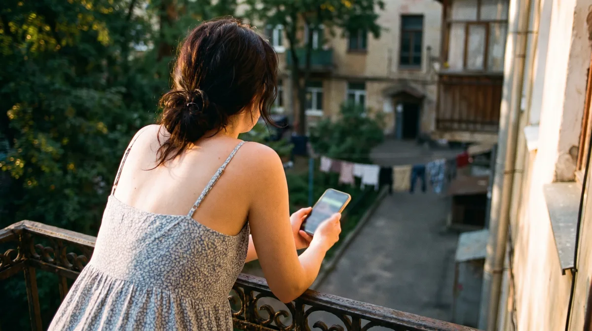 A young woman seen from behind on a balcony looking over a courtyard at dusk