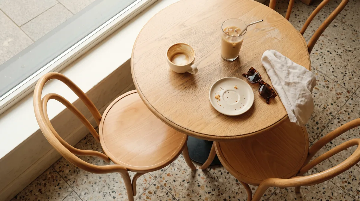 A café table seen from above, two cups and one chair pushed back, no one at the table
